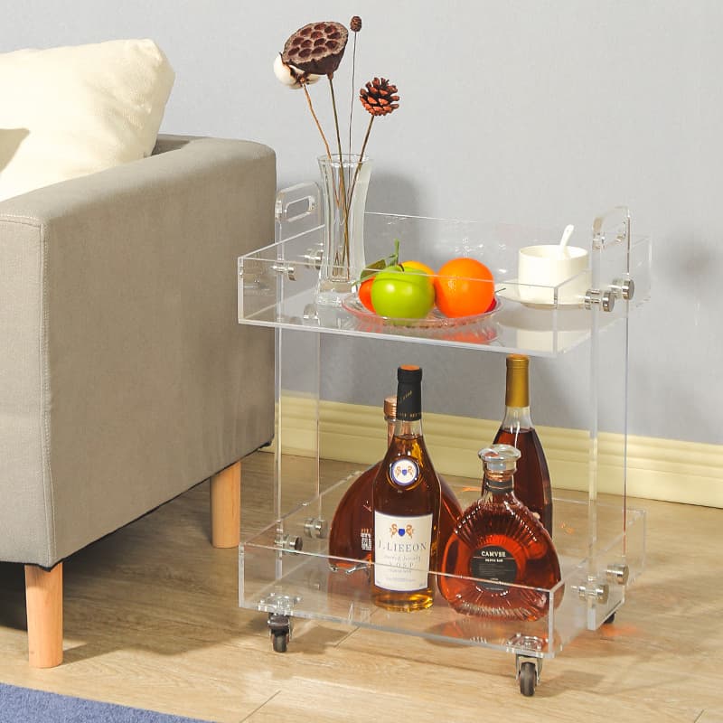 Clear acrylic bar cart holding liquor bottles and fruit, styled next to an armchair