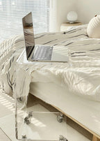 Acrylic C-table used as a bedside table, holding a laptop in a minimalist bedroom.