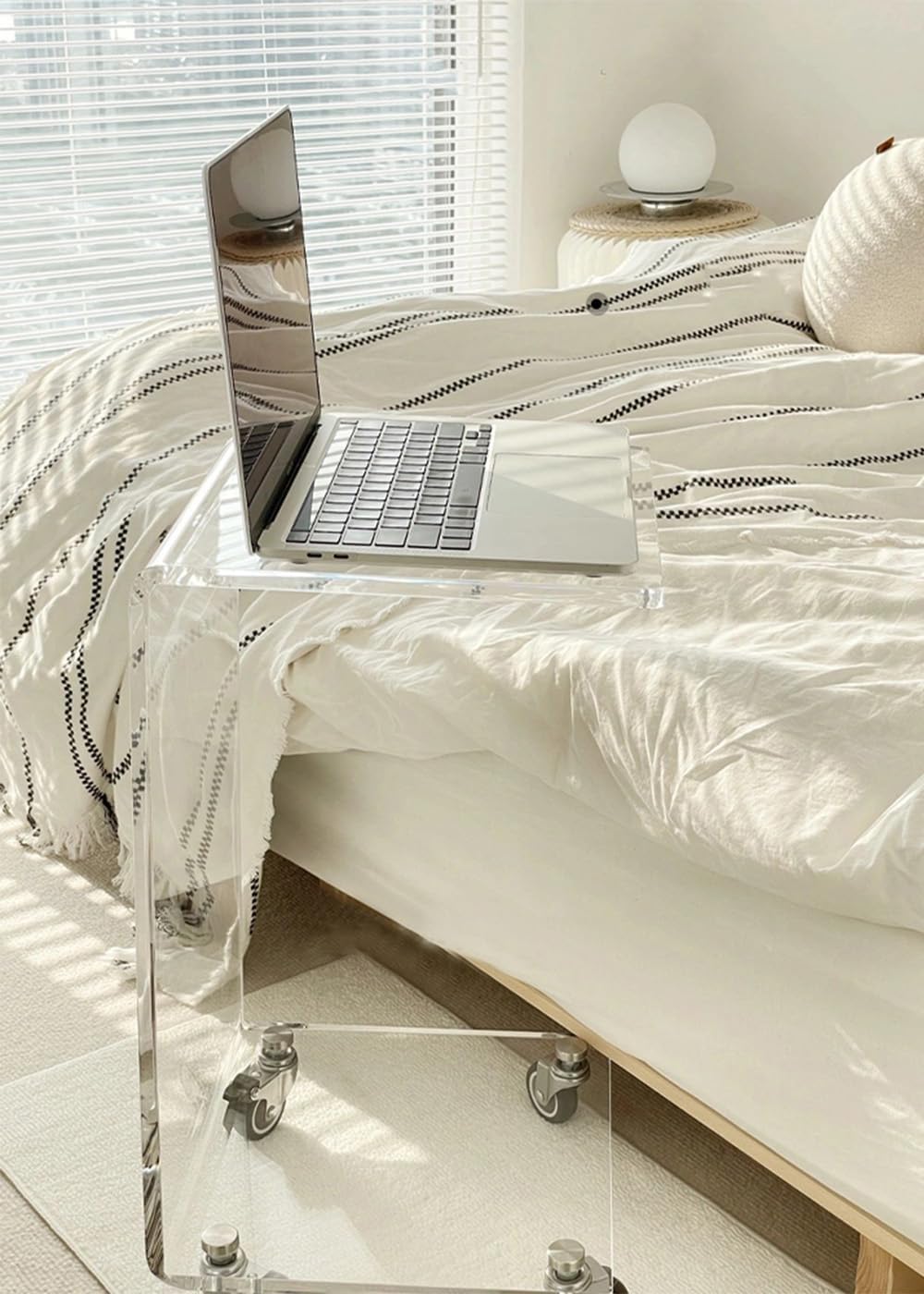 Acrylic C-table used as a bedside table, holding a laptop in a minimalist bedroom.