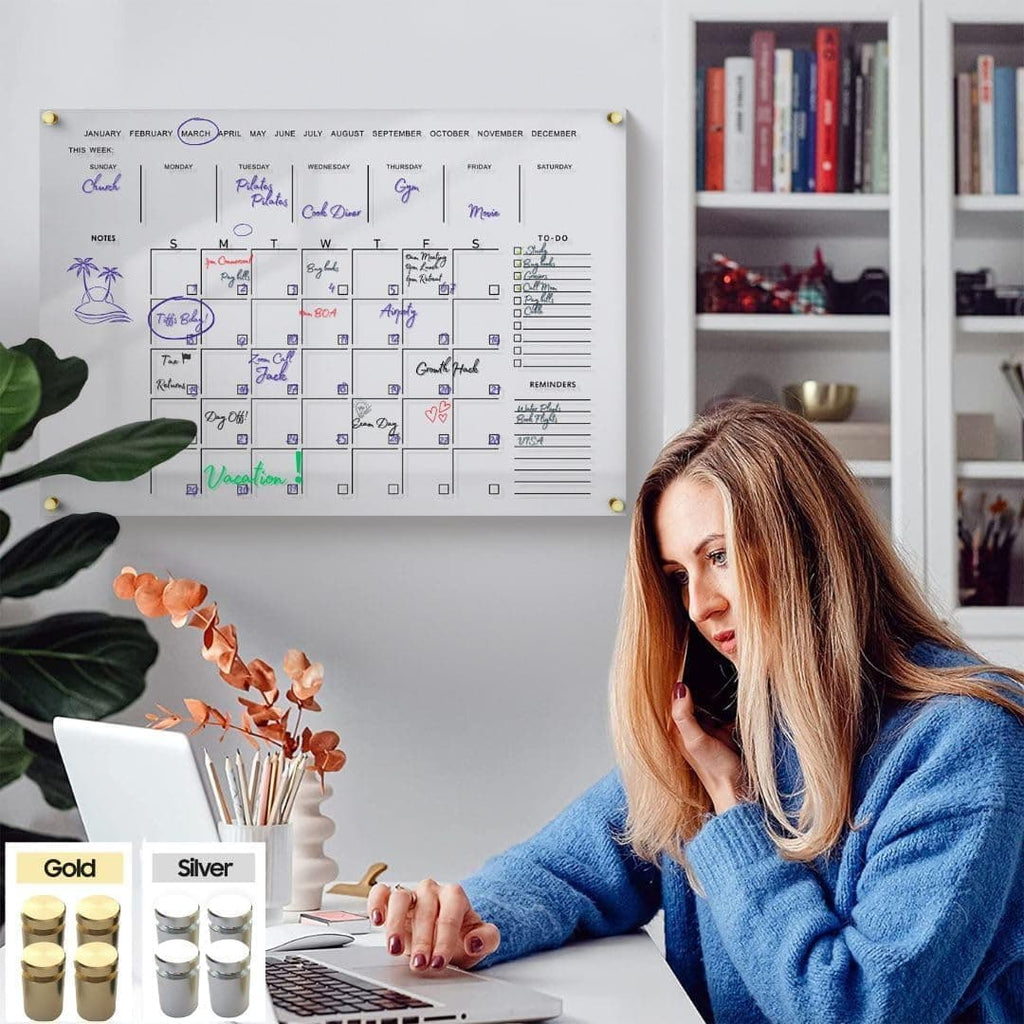 User interacting with a clear acrylic wall planner in a home office setting, with gold and silver hardware options