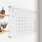 Clear acrylic wall calendar mounted in a minimalist hallway with wooden shelves
