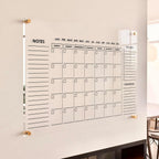 Clear acrylic monthly planner mounted on a living room wall, featuring a modern minimalist design