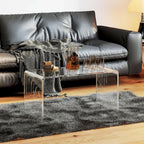 Clear acrylic coffee table next to a black leather sofa, styled with a pitcher of iced tea and glasses for a cozy look