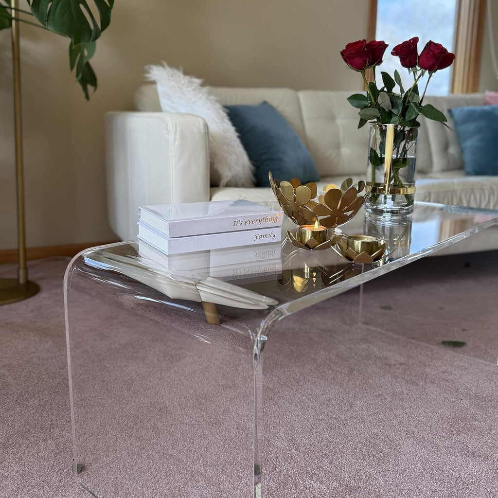 Clear acrylic coffee table styled with red roses, gold decor, and books, adding elegance to a cozy living room