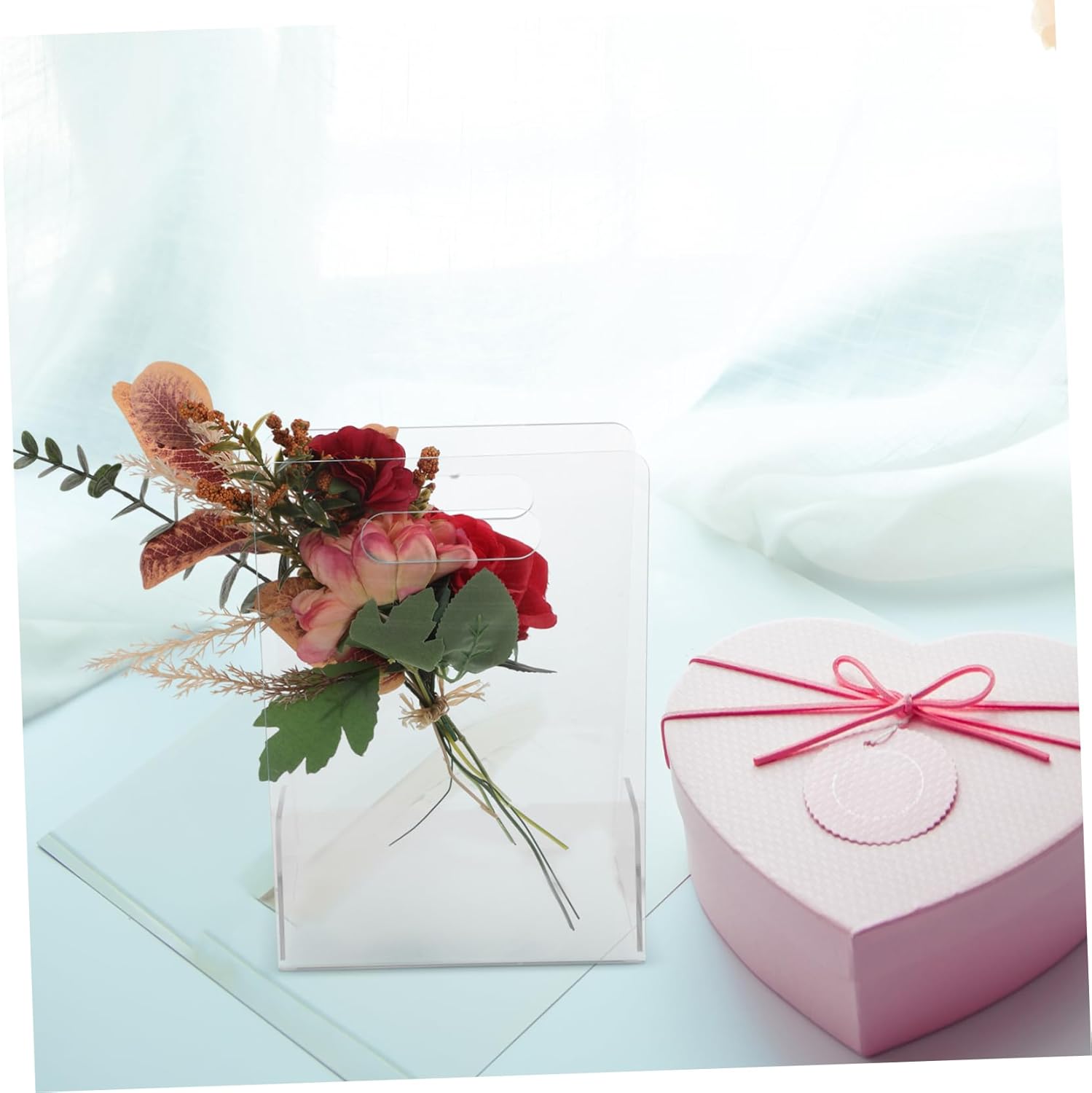 Clear acrylic flower box with a bouquet, next to a pink heart-shaped gift box