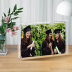 Clear Acrylic Magnetic Photo Frame on a wooden table, displaying a joyful graduation photo of three graduates, perfect for commemorating milestones