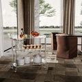Acrylic serving cart on a patio with a view, holding drinks and tableware for outdoor gatherings