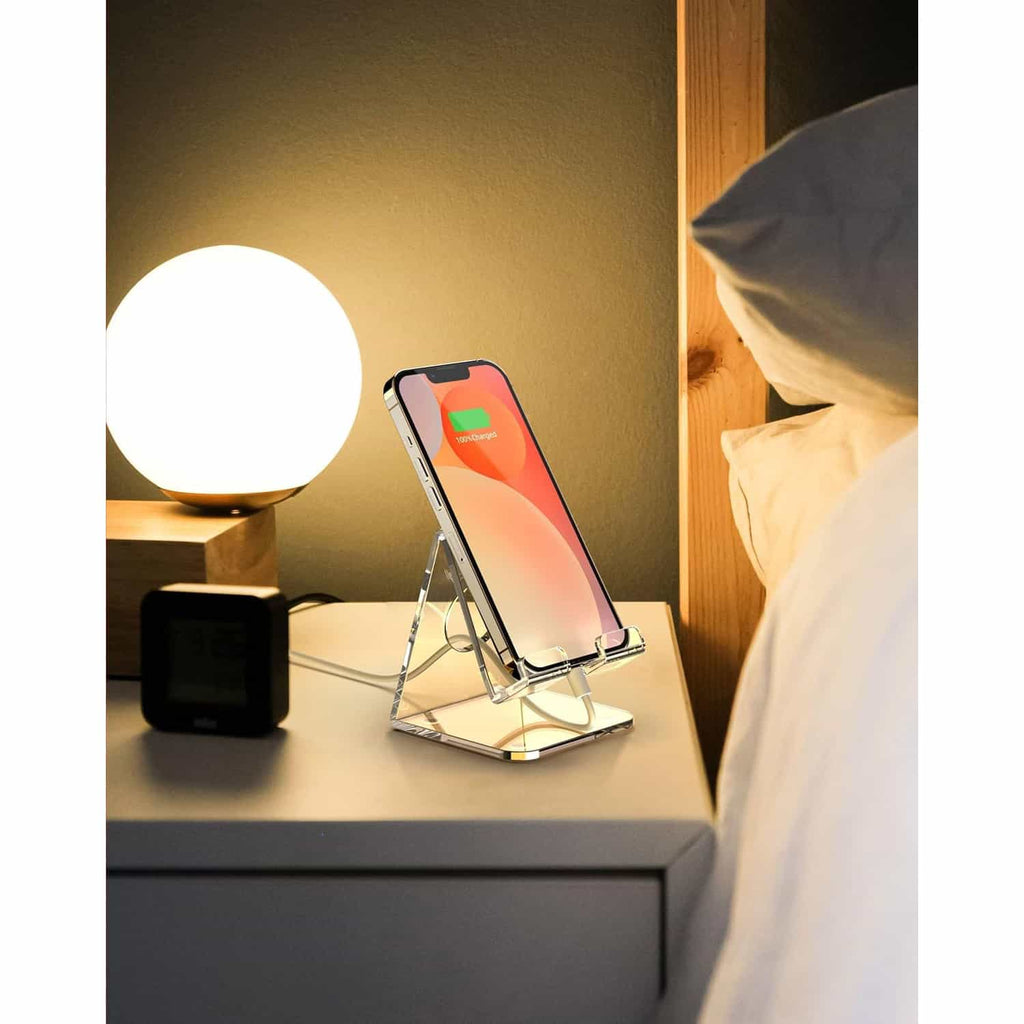 Clear acrylic phone stand used for charging an iPhone on a bedroom nightstand