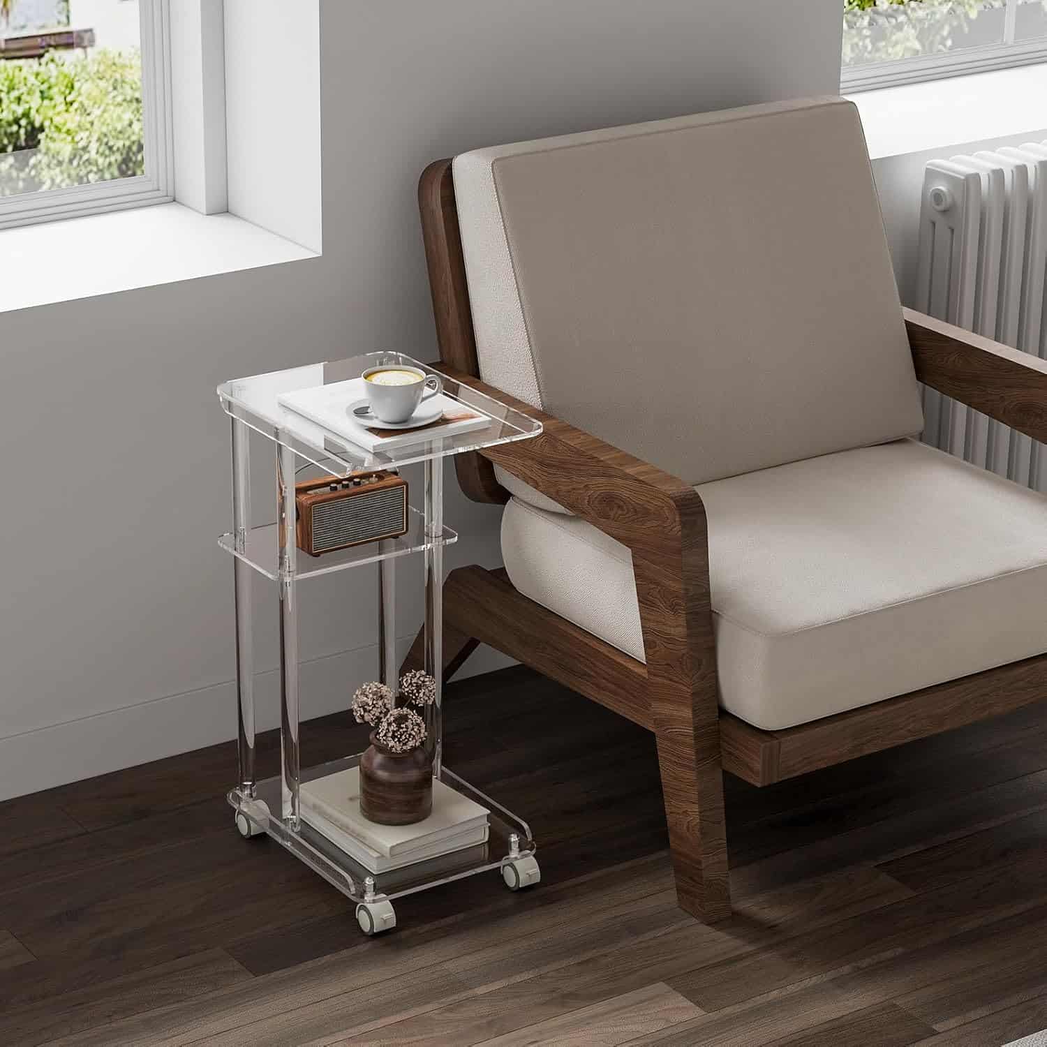 A 3-tier acrylic rolling side table placed next to a beige armchair, holding a coffee cup and radio