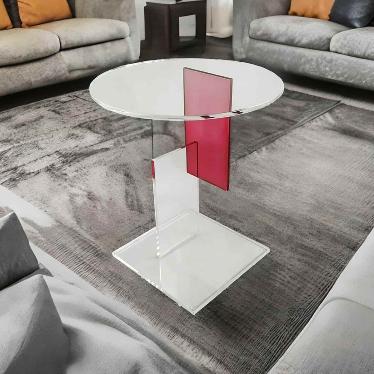 Clear acrylic round accent table with pink geometric support in living room interior, home furniture scene
