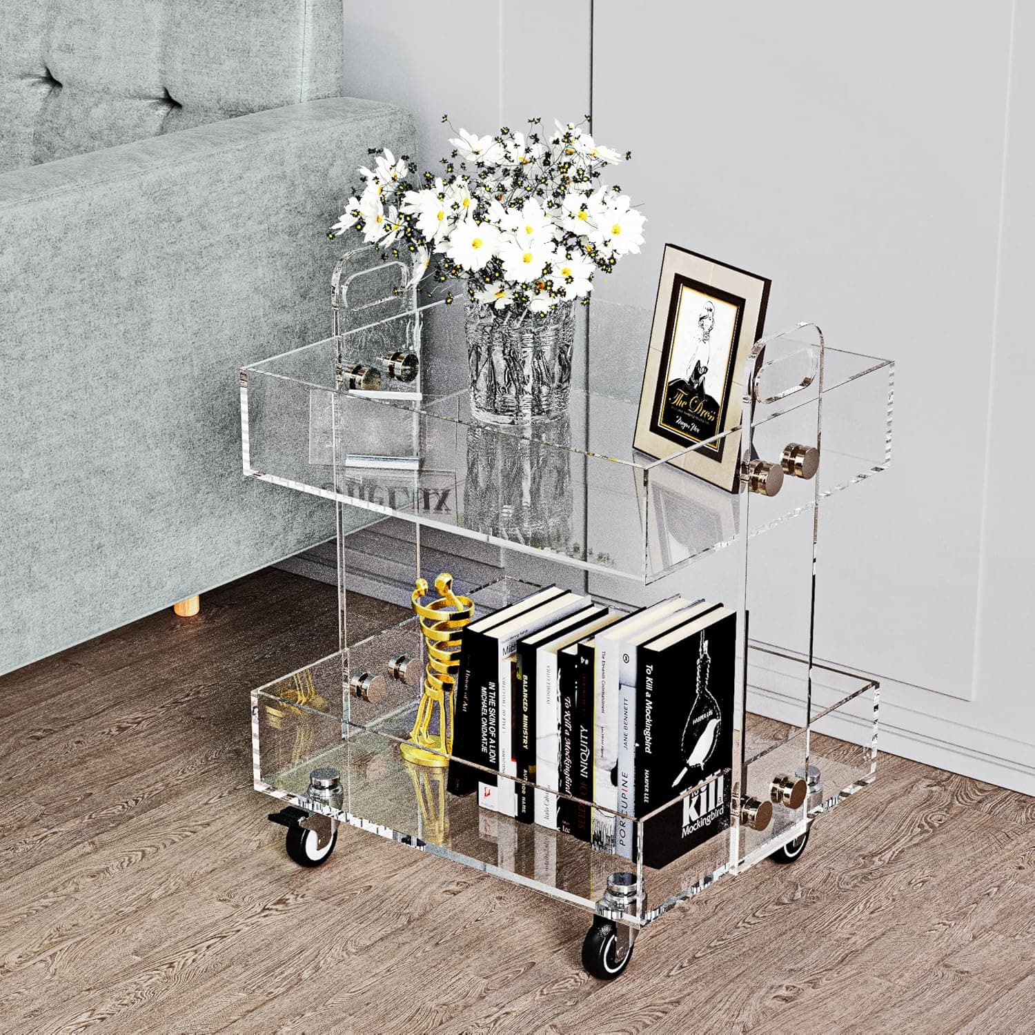 Clear acrylic rolling cart used as a side table in a living room, holding decor and books