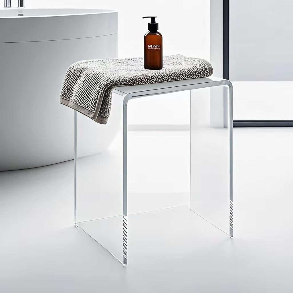 Transparent acrylic bench with towel and soap dispenser placed by a contemporary bathtub