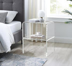 Clear acrylic side table used as a nightstand by the bed, paired with a table lamp and books in a modern bedroom