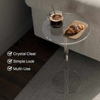 A clear acrylic side table by a sofa, holding a coffee cup and croissant, highlighting its crystal clear, simple, and multi-use design