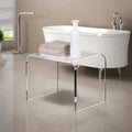 Transparent acrylic bench with towels and soap dispenser placed by a modern freestanding tub