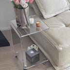 Clear acrylic C-shaped side table styled next to a beige sofa, holding a vase of flowers and candles.