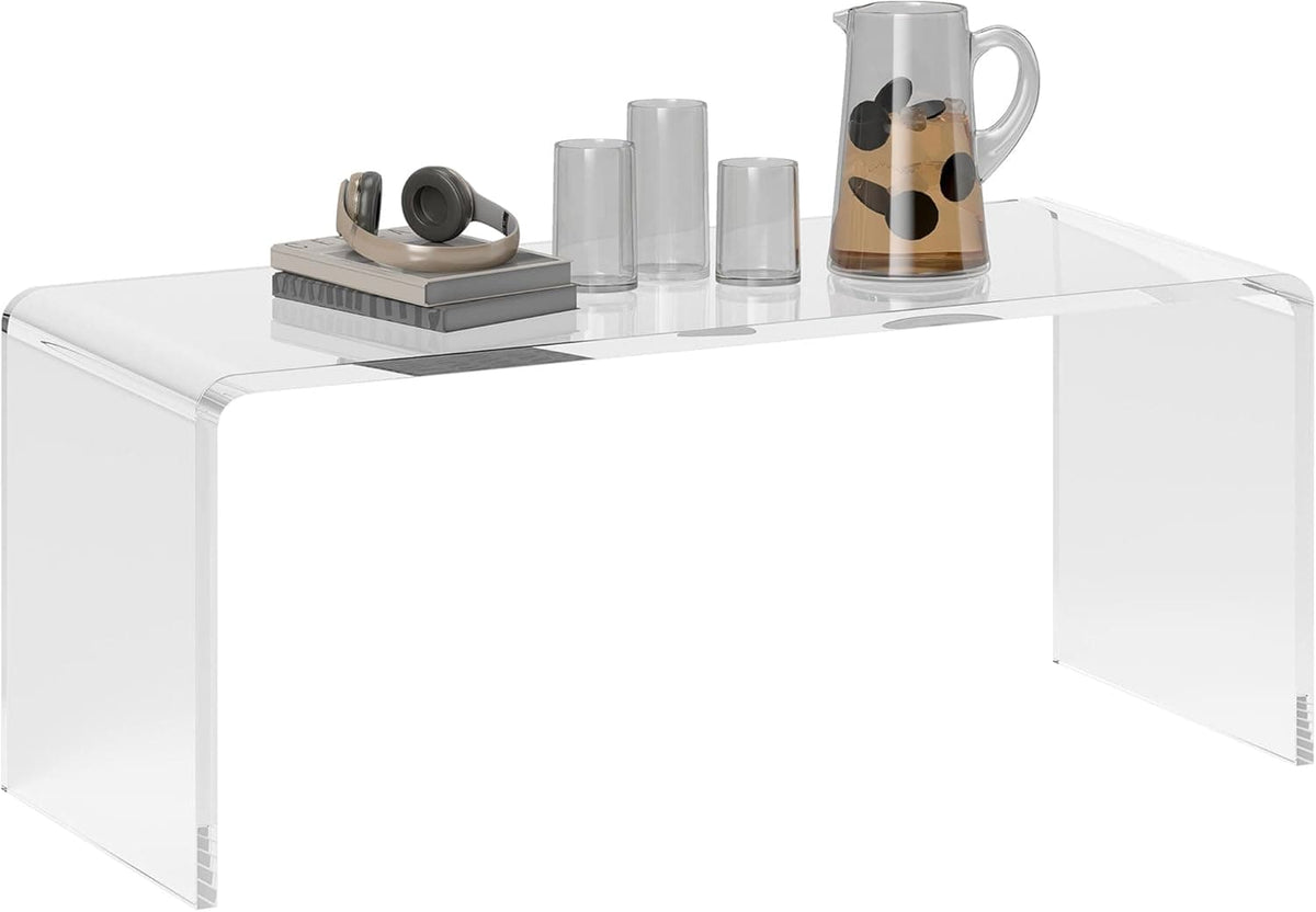 Clear acrylic waterfall coffee table styled with headphones, books, and a drink set, showcasing its sleek, transparent design